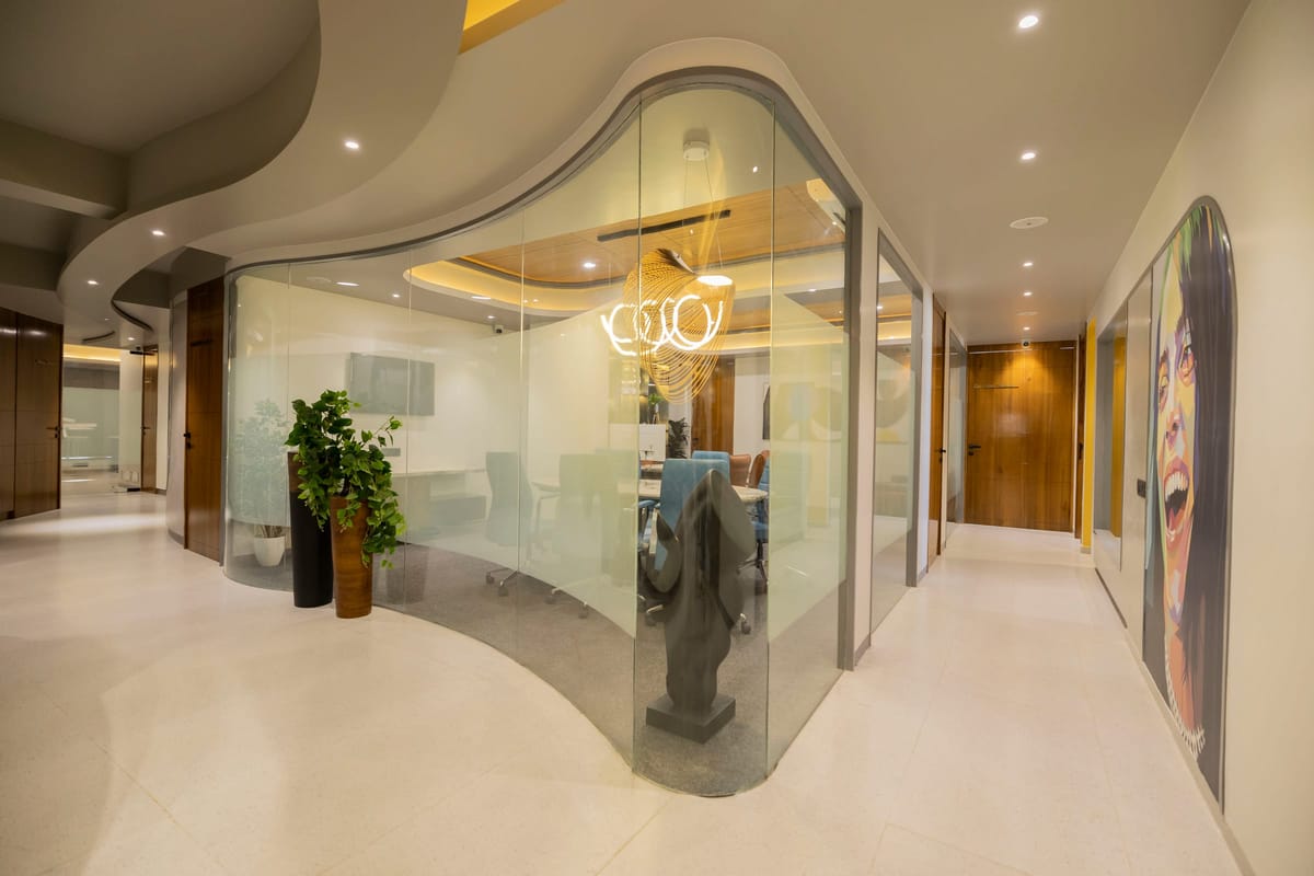 A curved glass-walled room along a corridor, with potted plants outside it