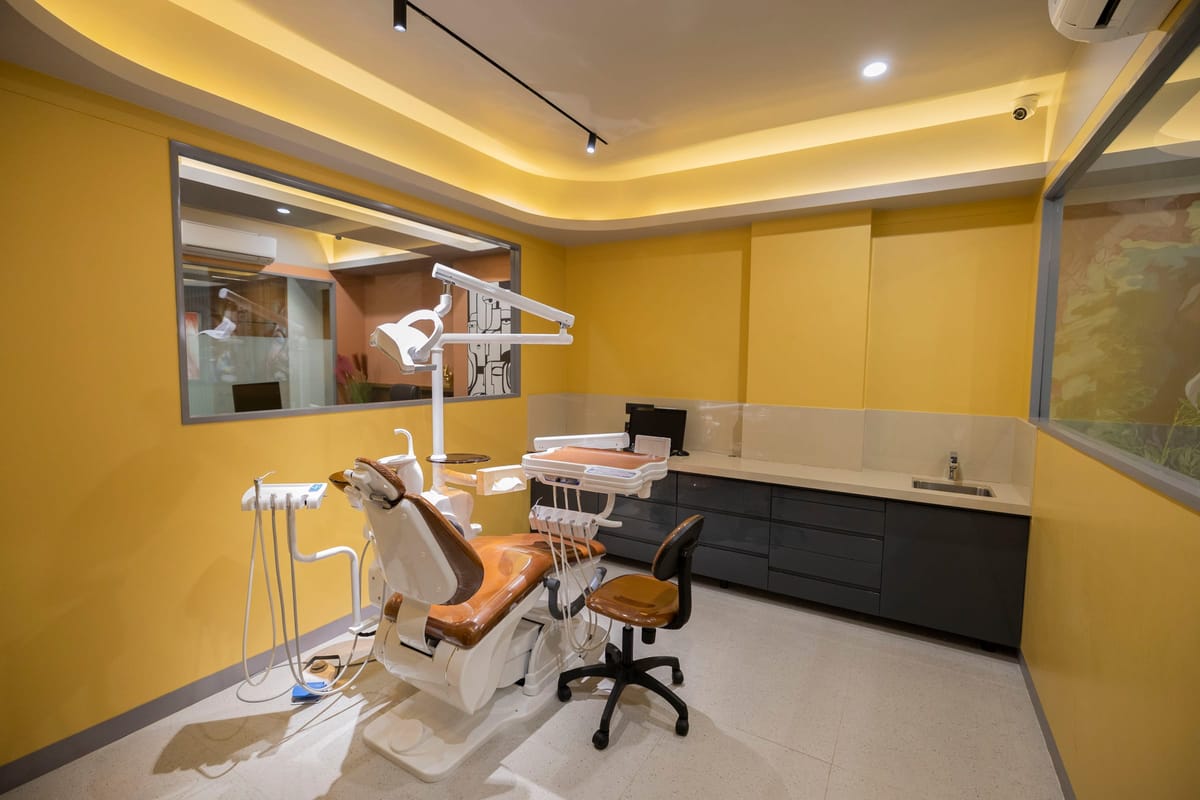 A treatment room in yellow tones, with a dental chair and a wall-mounted screen